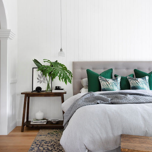 Designer bedroom featuring emerald green velvet cushions, timber bedside table and indoor plant.